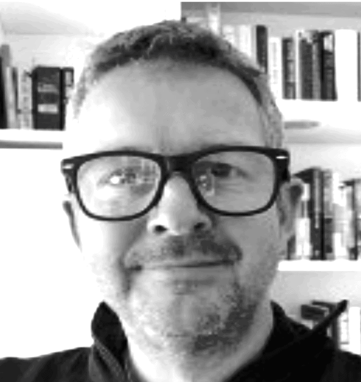 Professional portrait of a smiling CFO wearing glasses in an office with bookshelves in the background.