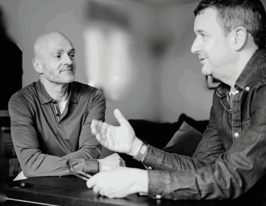 Two men engaged in a professional business discussion, shaking hands in a modern office setting, emphasizing collaboration and partnership.